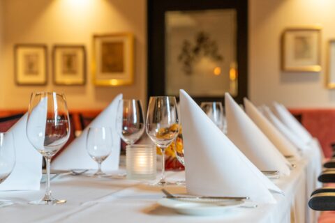 Elegant gedeckter Esstisch mit weißen Servietten, Weingläsern und einer brennenden Kerze in einem Restaurant.