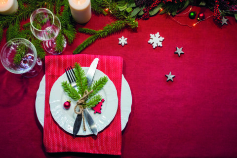 Festlich gedeckter Tisch mit Tellern, Besteck, Tannenzweigen, Kerzen und Weihnachtsschmuck.